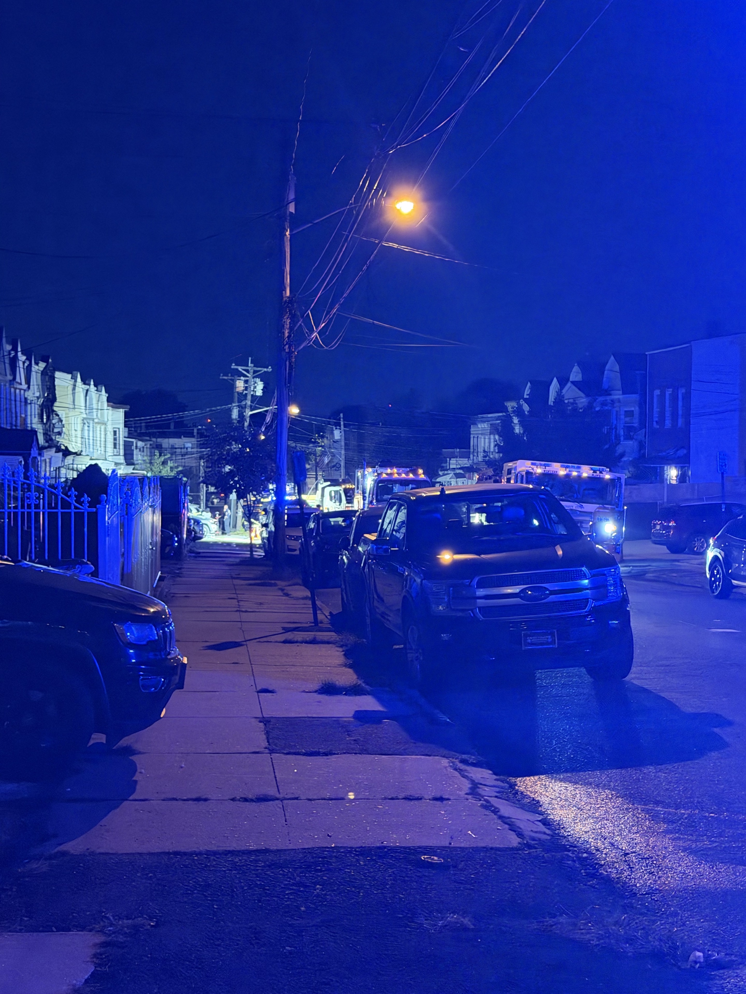 Nighttime view along the Boyd Avenue sidewalk, with parked SUVs and fire apparatus under blue emergency lighting.